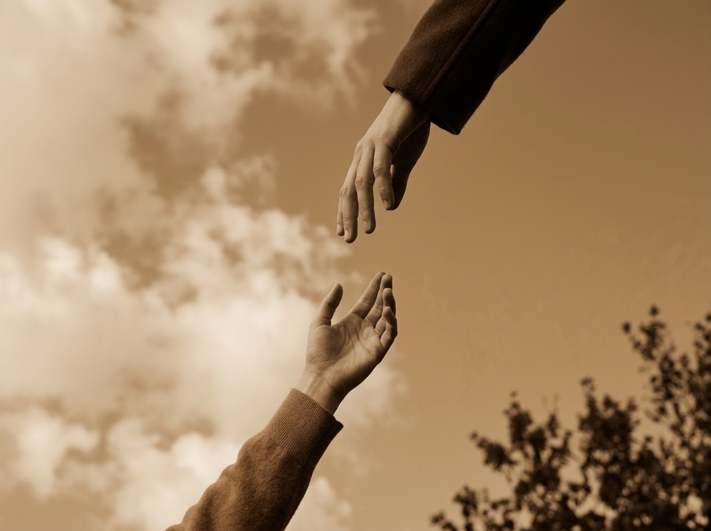 Two hands reaching toward each other against a sepia sky